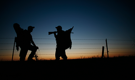 Two men crossing fence after hunting